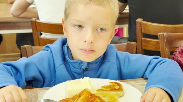 A young boy enjoys a warm breakfast inside a cruise ship restaurant on Lake Ladoga. He eats pancakes happily at the table. The pleasant meal brings feelings of sweet comfort and gentle joy.