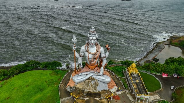 Aerial view of the massive Shiva statue at Murudeshwar Temple, featuring its silver finish and trident, set against the backdrop of the Arabian Sea in Murdeshwar, Karnataka, India.