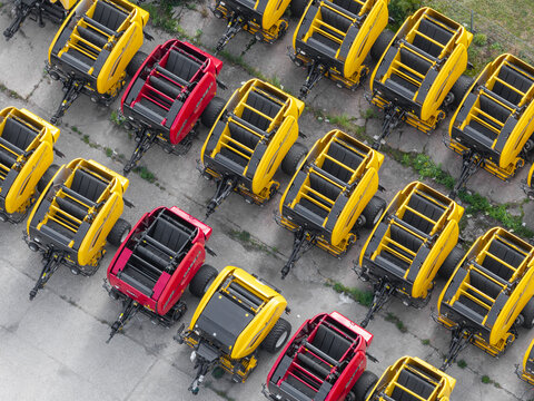 Plock, Poland - 10 September 2026: Aerial view of rows of yellow and red agricultural balers parked at a harvesting machinery manufacturing facility.
