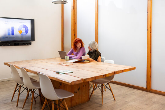 Young and mature women discuss business data in office