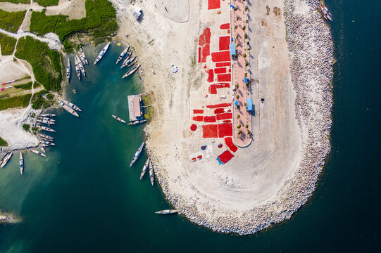 Bogura, Bangladesh - 06 March 2022: Aerial view of wooden boats docked along the riverbank, with vibrant red chilies spread out to dry on the concrete embankment.