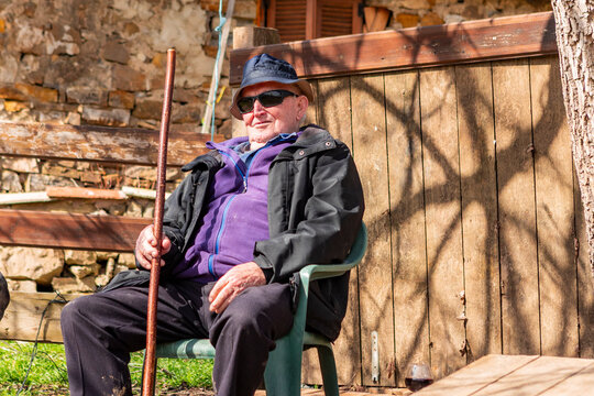 Elderly farmer resting with walking stick beside wooden shed