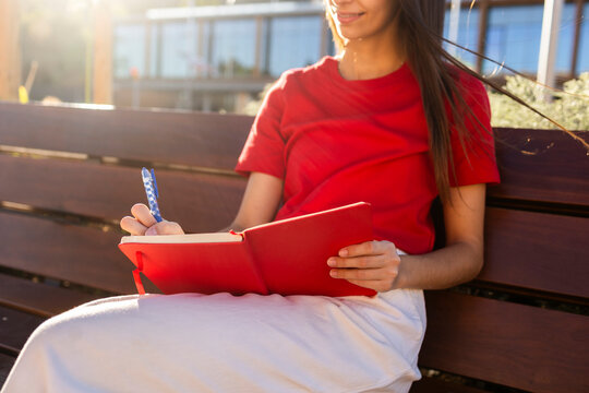 Woman writing in red notebook on park bench