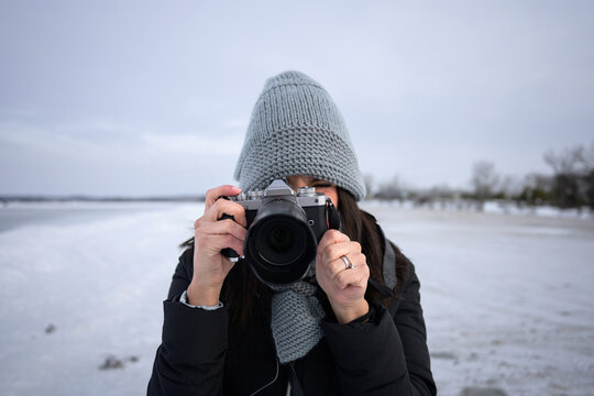 Woman hide face behind camera at Sylvan Lake in winter