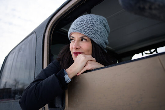 Thoughtful woman in beanie leaning from off-road vehicle