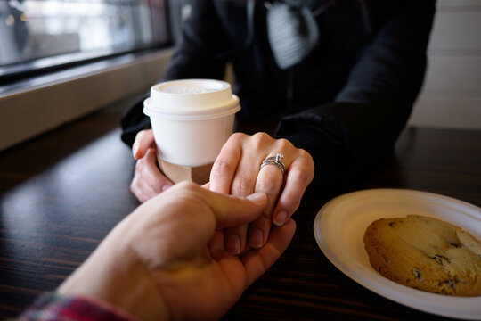 Woman with diamond engagement ring holds partner's hand