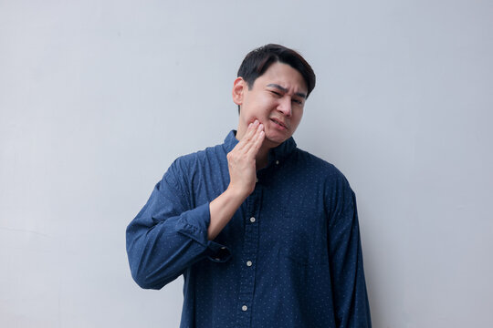 close up young asian man frown and use hand to massage on cheek after feeling pain or hurt from tmj muscle symptom at home for un healthy lifestyle and treatment concept