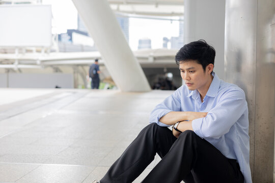 asian adult employee man sit on ground outside office with worry emotion after unemployed for economic global and business concept