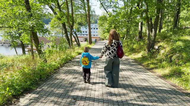 A woman and child walk hand in hand along a paved stone path. This serene stroll in Valaam, Lake Ladoga brings a calm, happy feeling of peaceful family harmony.