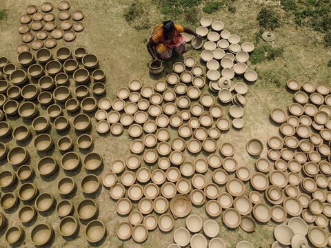 Joypurhat, Bangladesh - 28 September 2026: Aerial view of a woman arranging numerous handmade clay pots on the ground to dry in the sun.