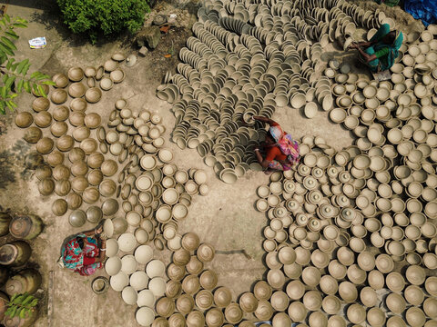 Joypurhat, Bangladesh - 28 September 2026: Aerial view of artisans arranging clay bowls on the ground to dry, showcasing traditional pottery craftsmanship.