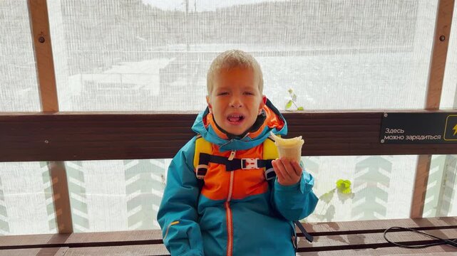 A happy boy eats ice cream while sitting on a bench on Valaam, Lake Ladoga. This delightful treat evokes a joyful, sweet, and heartwarming feeling.