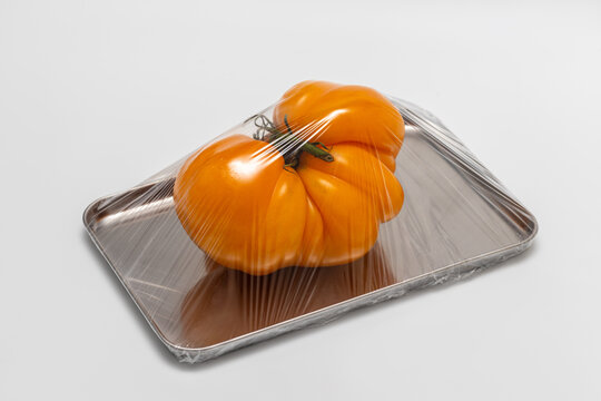 Orange heirloom tomato wrapped in plastic on metal tray