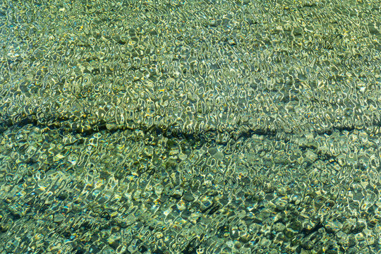Sunlit ripples over clear shallow water and pebble bed