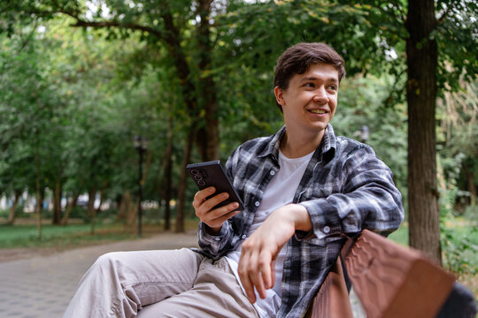 Smiling man use smartphone while relax in city park