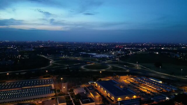 Cityscape at Dusk: An aerial view captures a sprawling urban landscape as twilight descends, with illuminated highways, industrial buildings. Milan, Italy