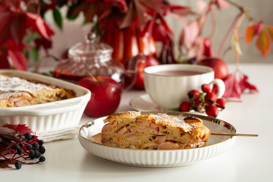 Warm apple pie slice served with tea and autumnal decoration on white background