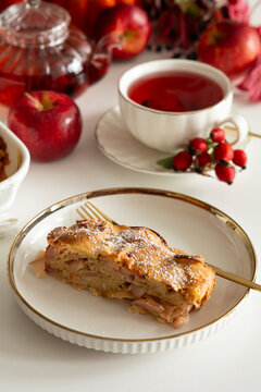 Slice of delicious apple strudel served with hot tea and fresh apples on a white table