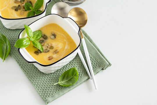 Two bowls of creamy pumpkin soup topped with seeds and basil leaves ready for serving.