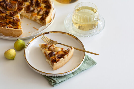 Delicious fig tart slice with fresh figs and a refreshing herbal tea on white table
