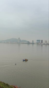 Aerial panoramic view of fishing boats sailing in the foreground with Quy Nhon city skyline in the background, Vietnam. Shot from Hai Minh peninsula featuring calm sea, coastal bay, and cityscape.