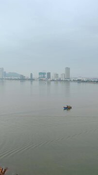 Aerial panoramic view of fishing boats sailing in the foreground with Quy Nhon city skyline in the background, Vietnam. Shot from Hai Minh peninsula featuring calm sea, coastal bay, and cityscape.