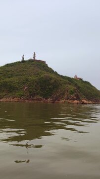 View from the water of Hai Minh peninsula featuring Phuoc Mai Lighthouse and Tran Hung Dao statue in Quy Nhon, Vietnam. Scenic sea view with historic coastal monuments and surrounding mountains.