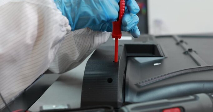 Close-up of a technician in blue gloves using a red screwdriver to assemble or repair a car dashboard in an automotive workshop.