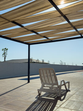 Empty patio chair beneath fabric pergola structure