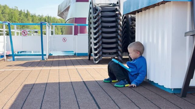 A cute boy plays on a tablet on a cruise ship deck at Valaam, Lake Ladoga. This cozy moment evokes a happy, peaceful, and joyful feeling.