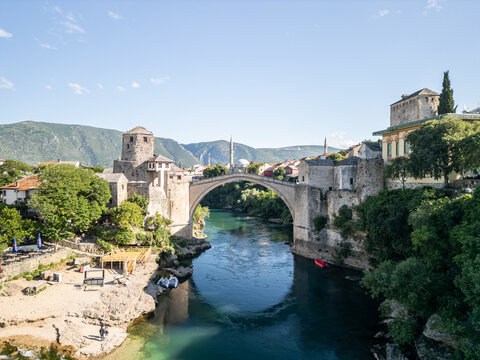 Mostar, Bosnia and Herzegovina - 28 May 2025: Aerial view of Old Bridge Mostar spanning the turquoise Neretva River, surrounded by historic stone architecture, lush trees, and rocky banks.