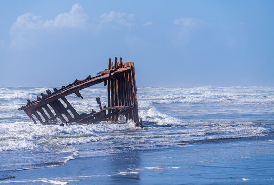 The rusted skeletal remains of the historic Peter Iredale shipwreck sit in ocean surf along the beach at Fort Stevens State Park in Oregon.