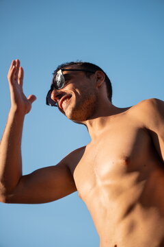 Shirtless man in sunglasses against a clear blue sky