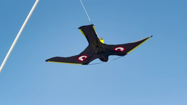 A black bird-shaped kite flies high in the bright blue sky. This joyful sight evokes a playful, carefree, and happy feeling.