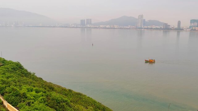 View from Phuoc Mai Lighthouse to Quy Nhon city with fishing boats in foreground, Vietnam. Scenic coastal view from Hai Minh peninsula with lighthouse, sea, mountains, and cityscape.