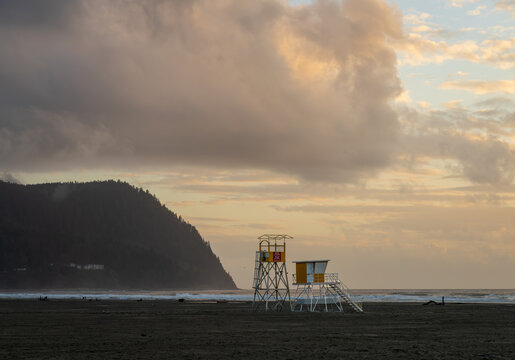 Lifeguard tower standing on the sandy shore of Seaside Beach with Tillamook Head on the Oregon coast at sunset.