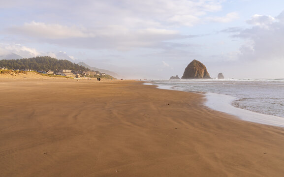 Haystack Rock rises beyond the wide sandy shoreline and Pacific surf at Cannon Beach in Clatsop County, Oregon.