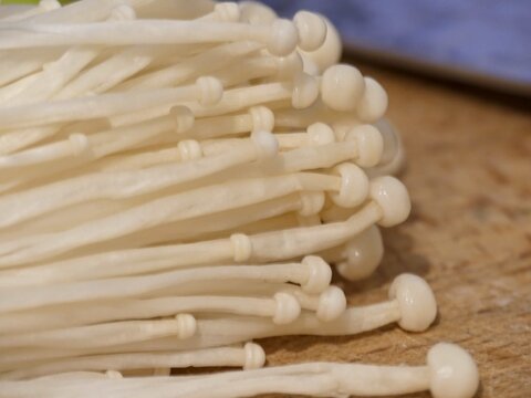 Fresh enoki mushrooms with long thin stems on wooden surface
