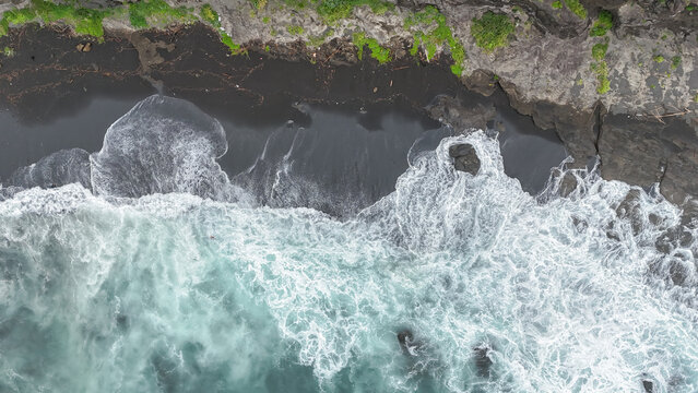 Miura, Kanagawa, Japan - 12 July 2026: Aerial view of the rugged coastline of Jogashima with crashing white waves against the dark volcanic sand beach and rocky cliffs.