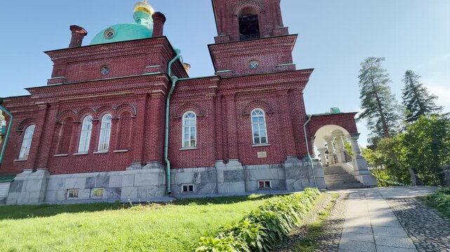 A historic red brick church stands along a scenic stone path on Valaam, Lake Ladoga. This magnificent religious landmark inspires a peaceful, serene, and majestic feeling.