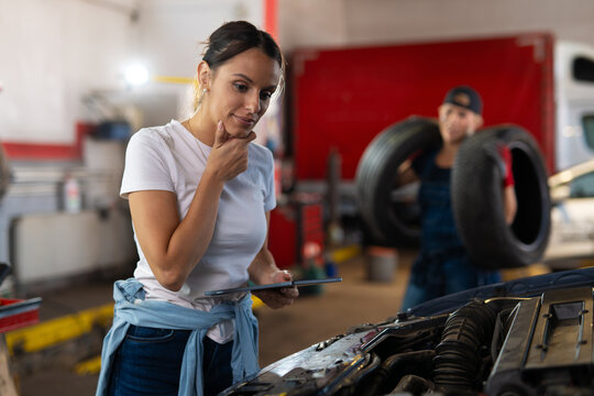 Female mechanic using digital tablet inspecting car engine