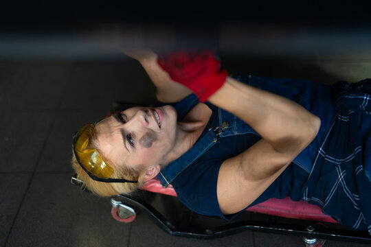 Woman mechanic working on car underside with tools