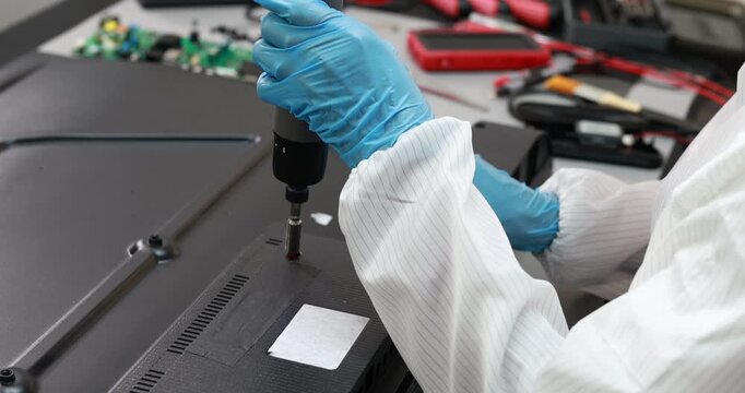 Technician wearing gloves uses a screwdriver to repair the back panel of a flat screen television in an electronics workshop