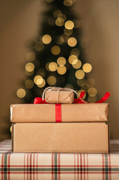 Stacked Christmas gifts with ribbon and tree bokeh