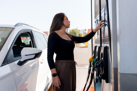 Woman operate gasoline pump at gas station beside car