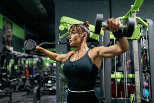 Woman perform dumbbell lateral raise exercise in gym