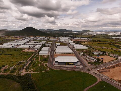Parque Industrial PyME, Mexico - 18 September 2026: Aerial view of the industrial park featuring rows of warehouses, paved roads, and surrounding green fields under a cloudy sky.