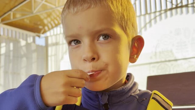 A young boy eats a sweet treat with a small spoon during a sunny trip in Valaam, Lake Ladoga. This quiet moment brings a calm, happy feeling of cozy vacation joy.