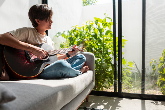 Young man play acoustic guitar beside sunlit window