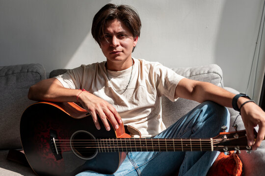 Young musician with acoustic guitar relaxing on sofa
